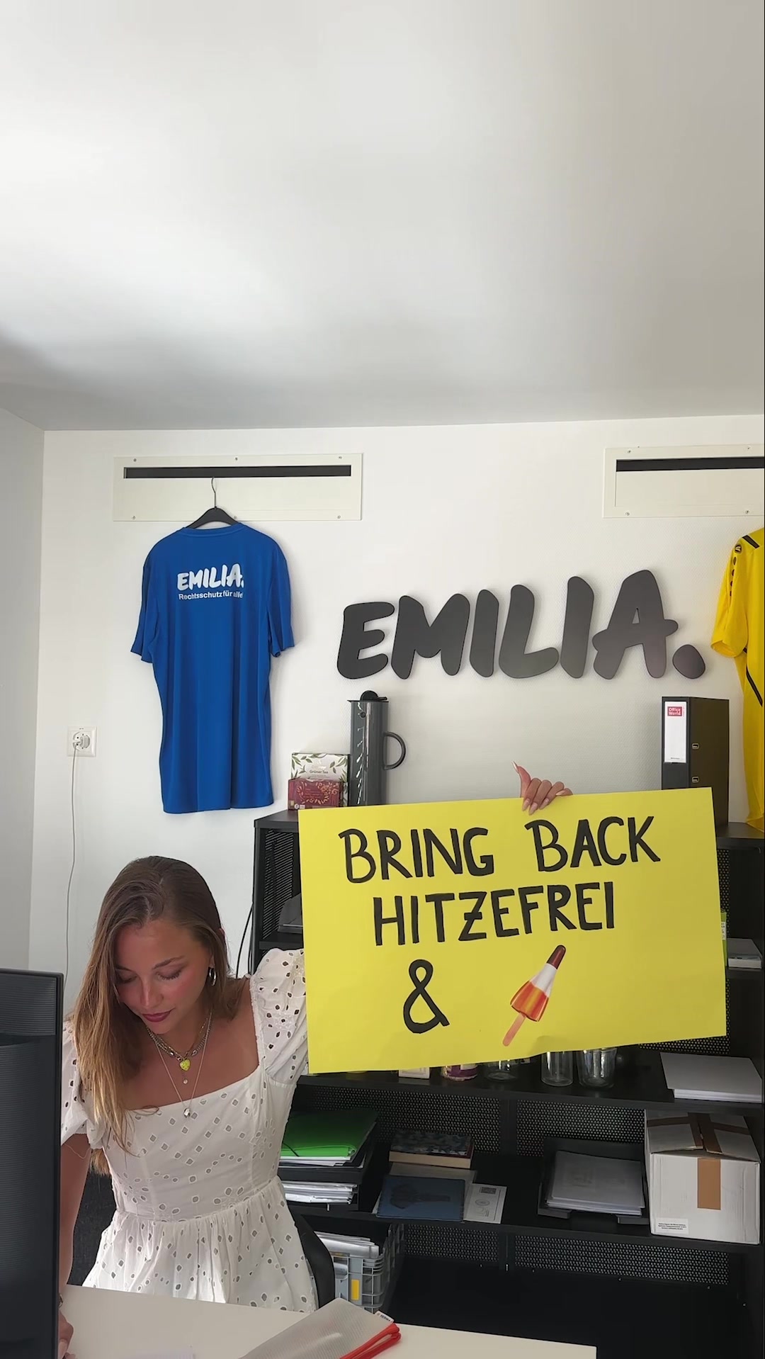 Eine Frau sitzt mit einem Schild an einem Schreibtisch.